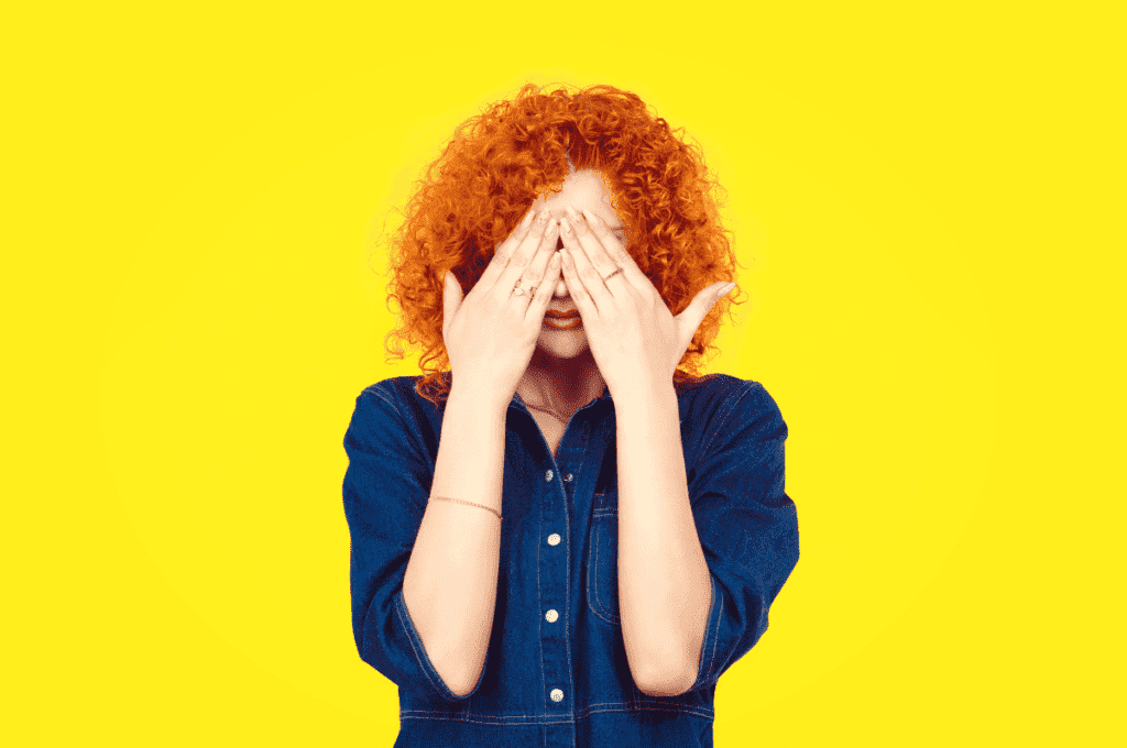 woman with red hair covers her face with hands